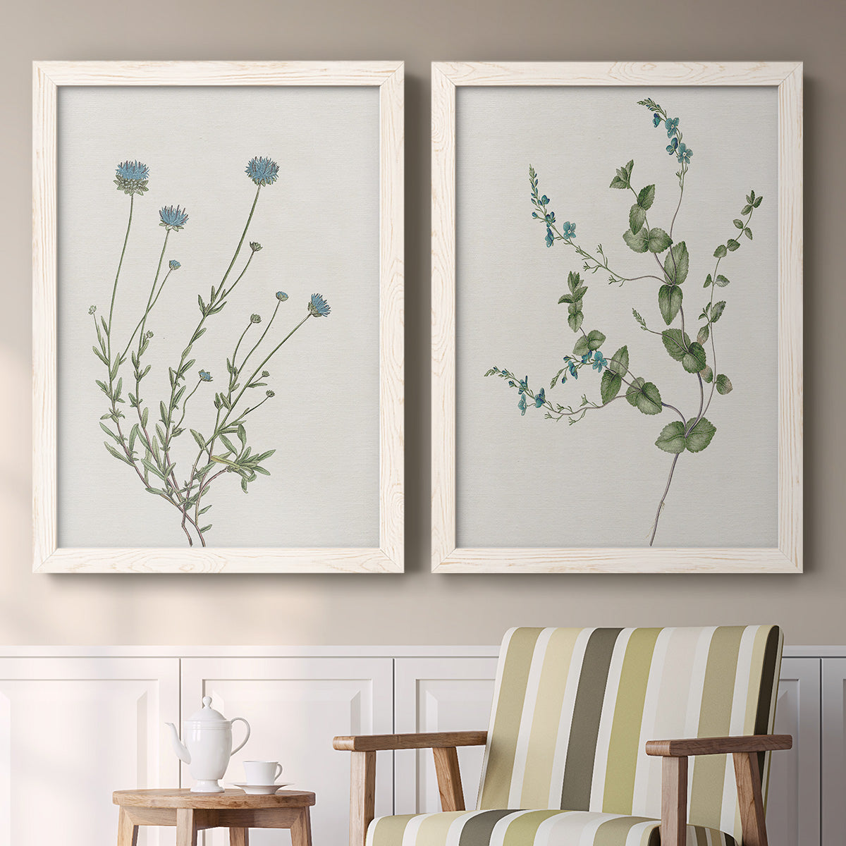 Set of two white barnwood framed canvas prints depicting two rustic minimalist botanical studies featuring delicate wildflower and leafy stems above a sideboard in a cozy sitting room.