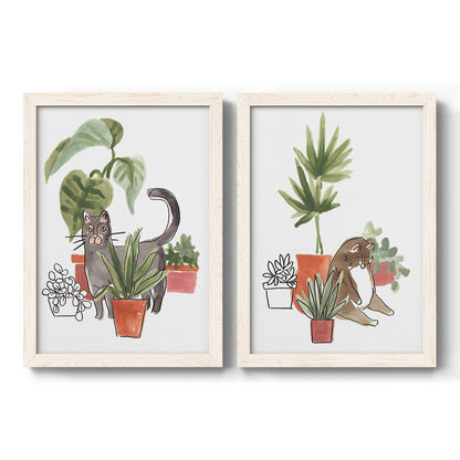 Set of two white barnwood framed canvas prints featuring two whimsical botanical animal illustrations featuring cats tucked among collections of potted houseplants.
