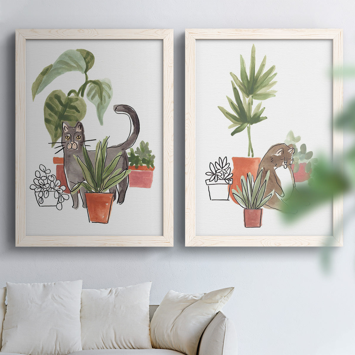 Set of two white barnwood framed canvas prints depicting curious felines, terracotta pots, succulents, and leafy stems arranged across two complementary compositions above a sofa in a bright living space.