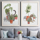 Set of two white barnwood framed canvas prints depicting paired whimsical botanical animal illustrations with curious felines, terracotta pots, succulents, and leafy stems above a sofa in a contemporary living room.