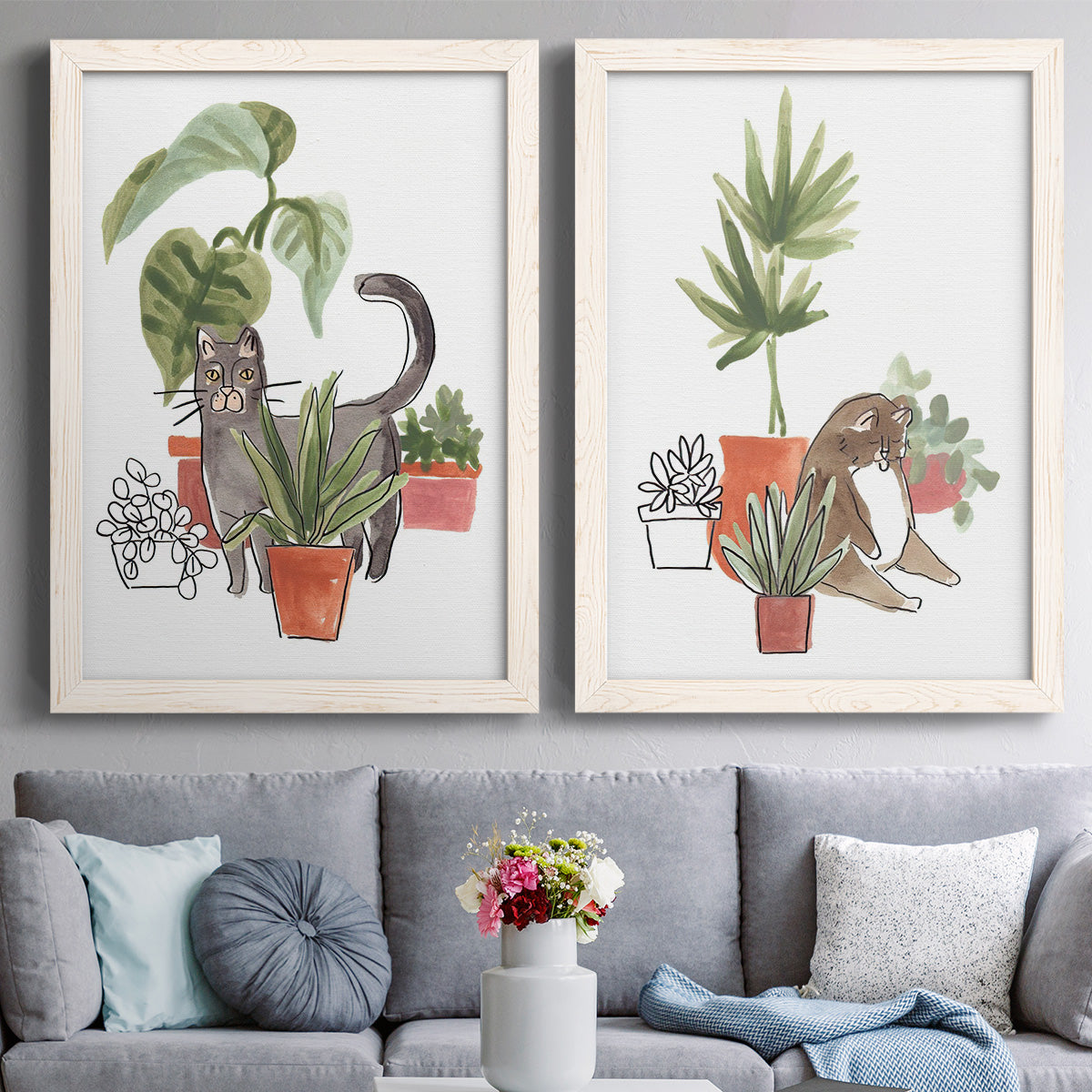 Set of two white barnwood framed canvas prints depicting paired whimsical botanical animal illustrations with curious felines, terracotta pots, succulents, and leafy stems above a sofa in a contemporary living room.
