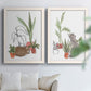 Set of two white barnwood framed canvas prints depicting curious felines, terracotta pots, succulents, and leafy stems arranged across two complementary compositions above a sofa in a bright living space.