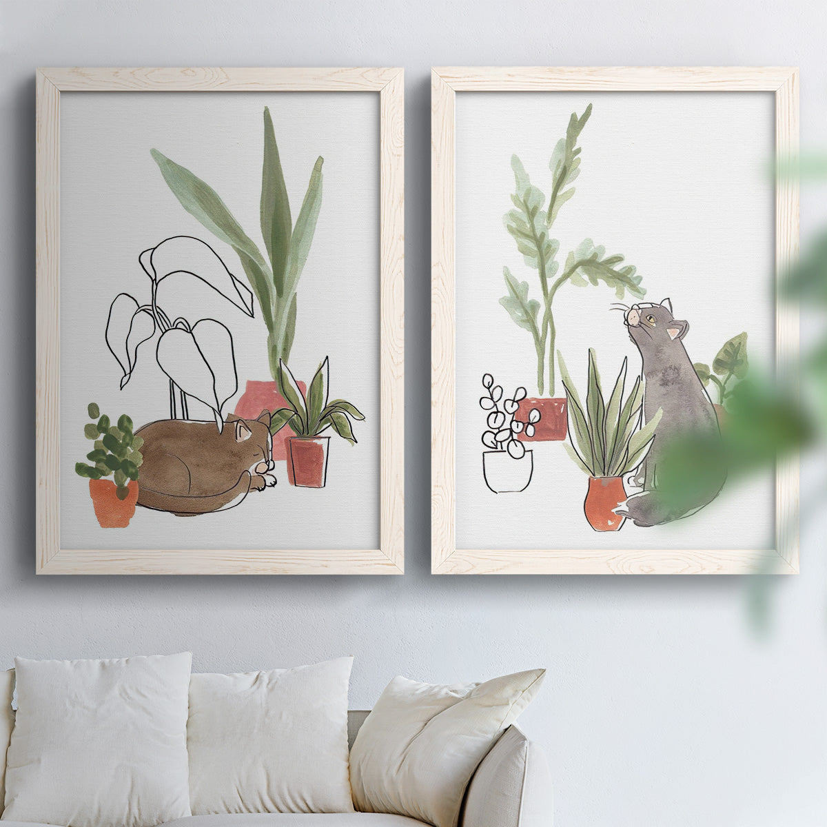 Set of two white barnwood framed canvas prints depicting curious felines, terracotta pots, succulents, and leafy stems arranged across two complementary compositions above a sofa in a bright living space.