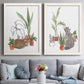 Set of two white barnwood framed canvas prints depicting paired whimsical botanical animal illustrations with curious felines, terracotta pots, succulents, and leafy stems above a sofa in a contemporary living room.