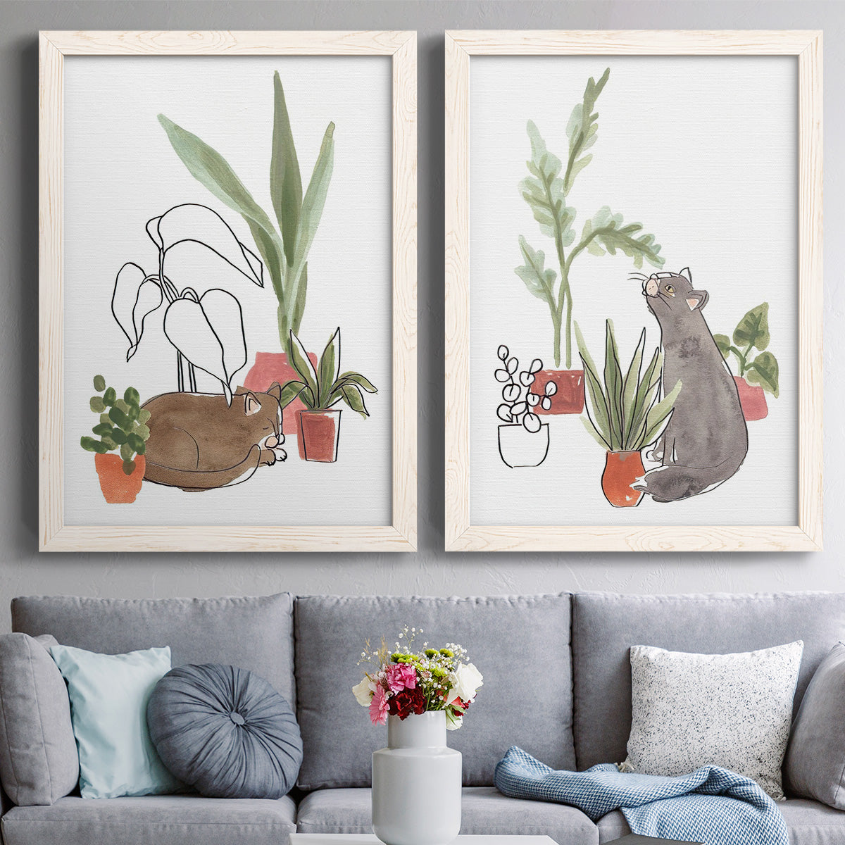 Set of two white barnwood framed canvas prints depicting paired whimsical botanical animal illustrations with curious felines, terracotta pots, succulents, and leafy stems above a sofa in a contemporary living room.