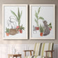 Set of two white barnwood framed canvas prints depicting two whimsical botanical animal illustrations featuring cats tucked among collections of potted houseplants above a sideboard in a cozy sitting room.