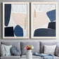 Set of two white barnwood framed canvas prints depicting paired minimalist color-block abstracts with rounded dark forms, pale sand fields, and clean modern edges above a sofa in a contemporary living room.