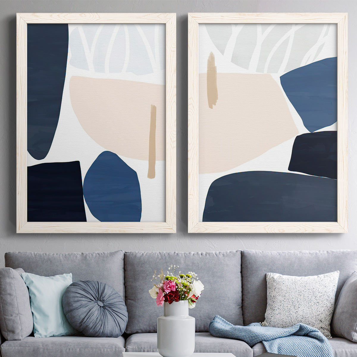 Set of two white barnwood framed canvas prints depicting paired minimalist color-block abstracts with rounded dark forms, pale sand fields, and clean modern edges above a sofa in a contemporary living room.