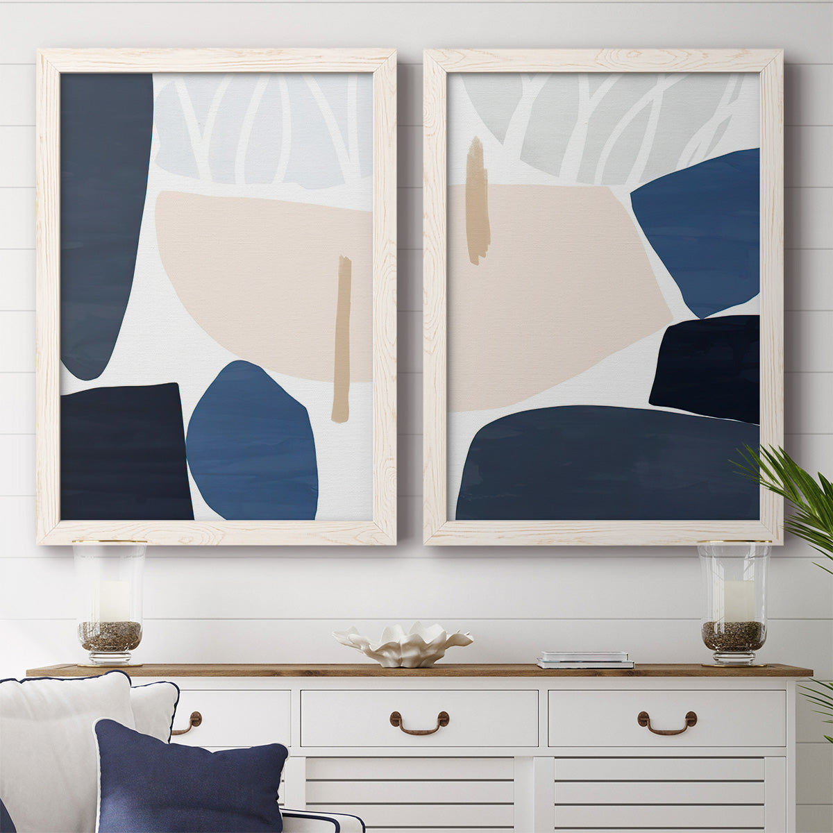 Set of two white barnwood framed canvas prints depicting a coordinated art pair of large navy cream and beige organic geometric shapes rendered as minimalist color-block abstracts above a dining room sideboard.