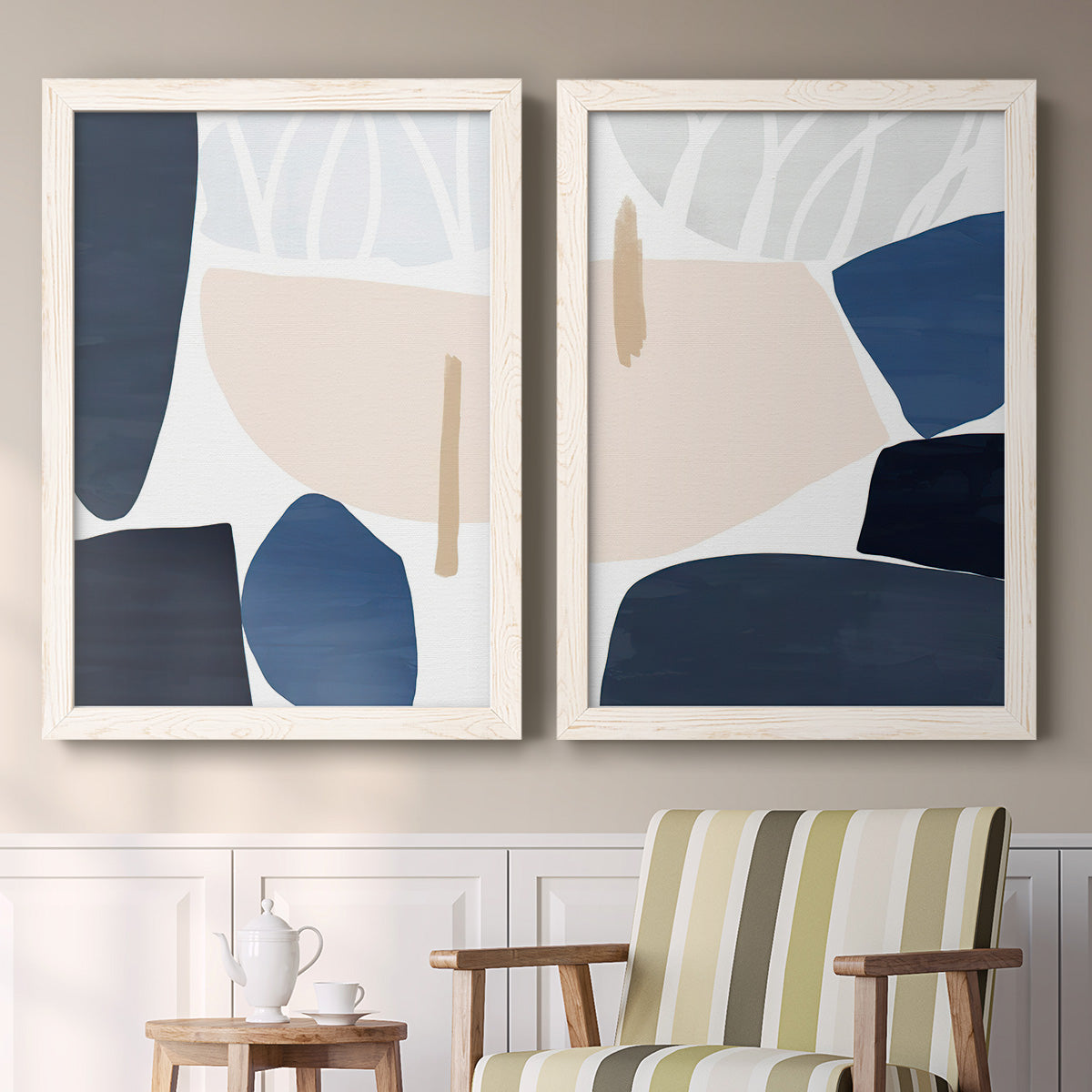 Set of two white barnwood framed canvas prints depicting two minimalist color-block abstracts featuring large navy cream and beige organic geometric shapes above a sideboard in a cozy sitting room.