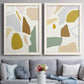 Set of two white barnwood framed canvas prints depicting paired pastel geometric abstracts with rounded color patches, thin white boundaries, and airy cream grounds above a sofa in a contemporary living room.