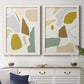 Set of two white barnwood framed canvas prints depicting a coordinated art pair of soft mustard sage gray and white irregular shapes rendered as pastel geometric abstracts above a dining room sideboard.