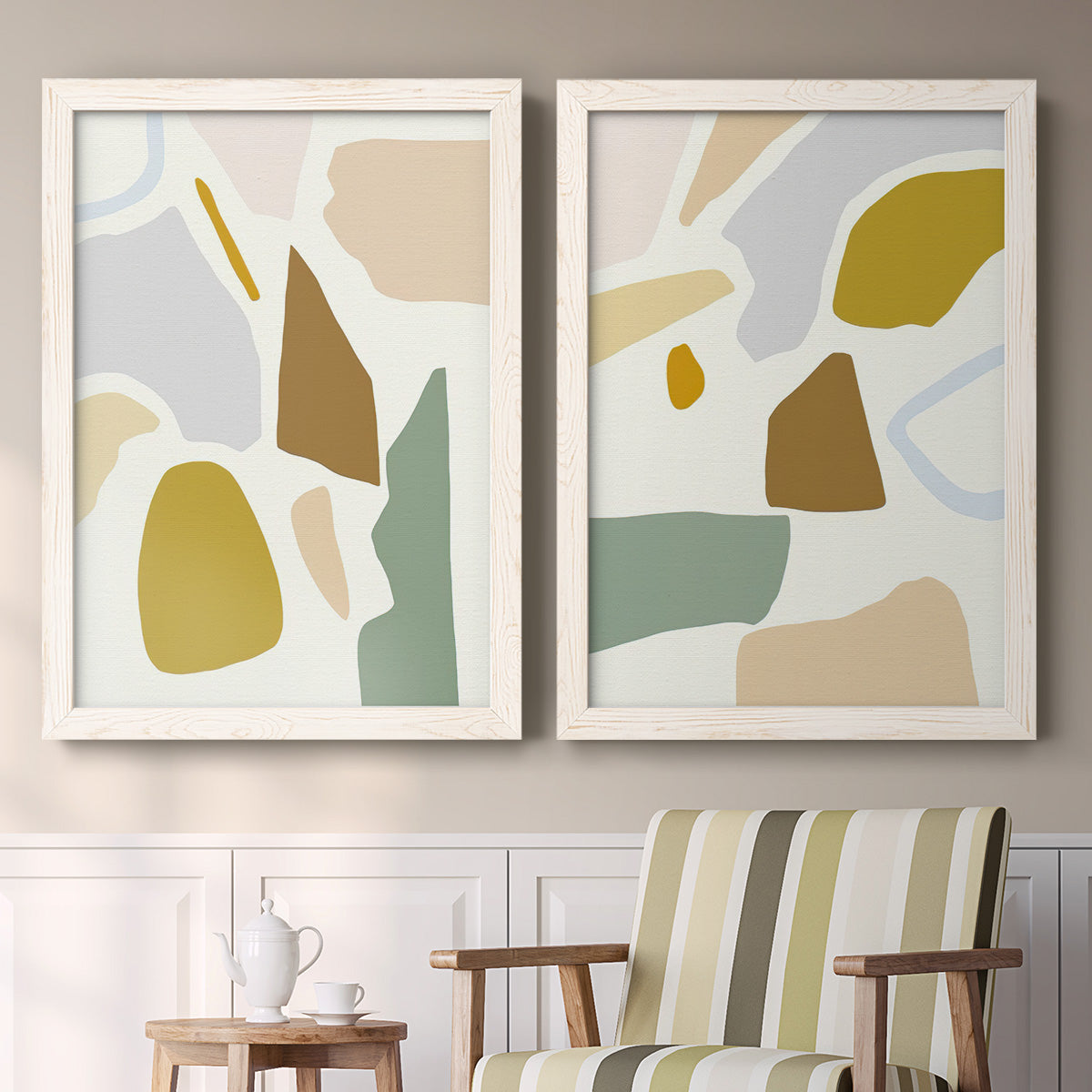 Set of two white barnwood framed canvas prints depicting two pastel geometric abstracts featuring soft mustard sage gray and white irregular shapes above a sideboard in a cozy sitting room.