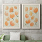 Set of two white barnwood framed canvas prints depicting a coordinated art pair of loose peach-orange tulip-like blossoms rendered as airy watercolor floral paintings above a sofa in a modern living room.