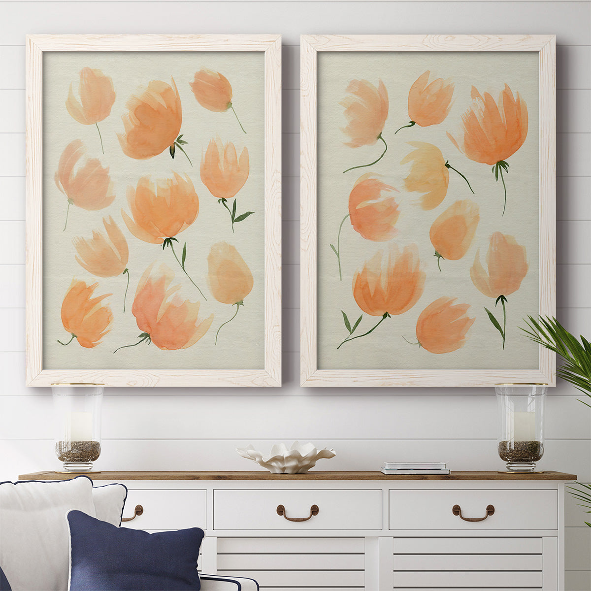 Set of two white barnwood framed canvas prints depicting a coordinated art pair of loose peach-orange tulip-like blossoms rendered as airy watercolor floral paintings above a dining room sideboard.