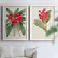 Set of two white barnwood framed canvas prints depicting large green leaves, red blossoms, and archival cream paper arranged across two complementary compositions above a sofa in a bright living space.