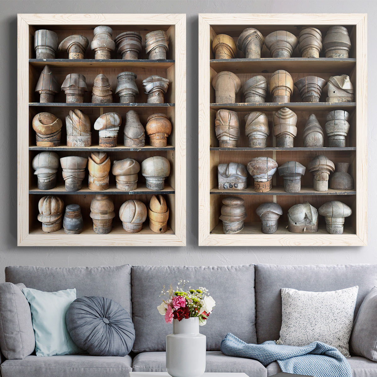 Set of two white barnwood framed canvas prints depicting paired fashion-object photography with rows of carved hat blocks, warm wood tones, and workshop shelving above a sofa in a contemporary living room.