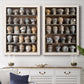Set of two white barnwood framed canvas prints depicting a coordinated art pair of shelves filled with wooden hat forms rendered as fashion-object photography above a dining room sideboard.