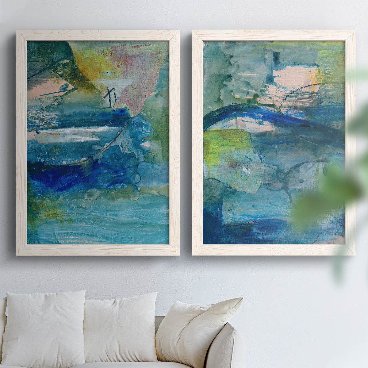 Set of two white barnwood framed canvas prints depicting broad strokes, scratched lines, and luminous color passages arranged across two complementary compositions above a sofa in a bright living space.