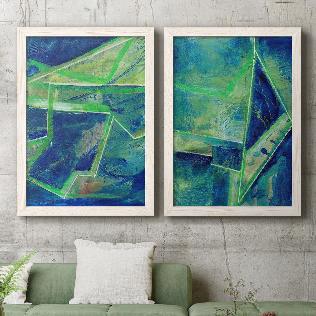 Set of two white barnwood framed canvas prints depicting a coordinated art pair of interlocking blue and green angular forms rendered as textured geometric abstracts above a sofa in a modern living room.