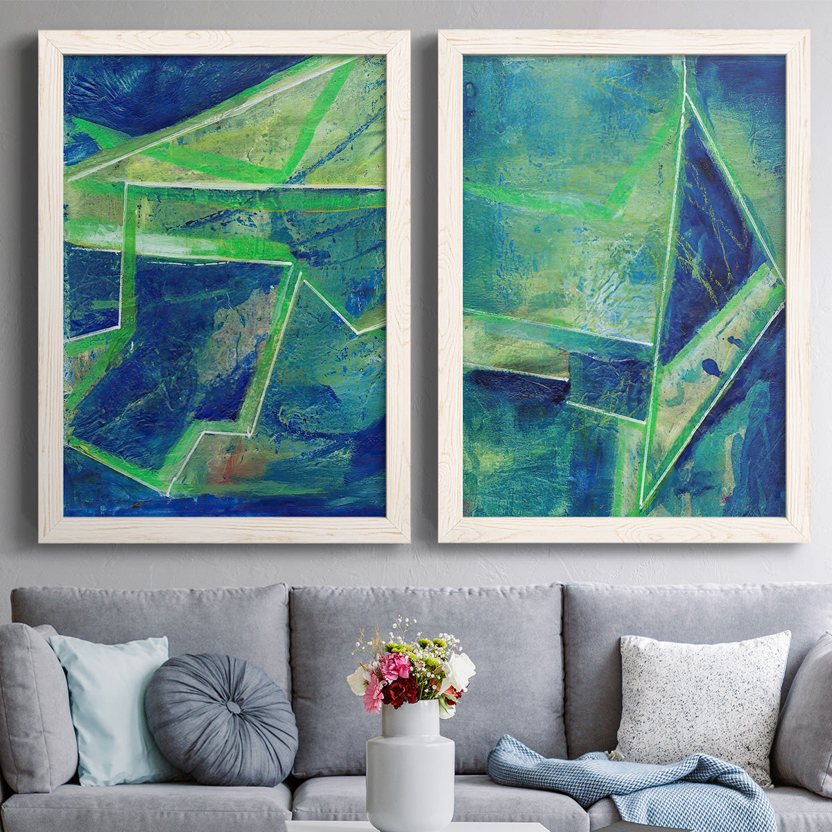 Set of two white barnwood framed canvas prints depicting paired textured geometric abstracts with deep cobalt fields, bright green edges, and layered linear facets above a sofa in a contemporary living room.