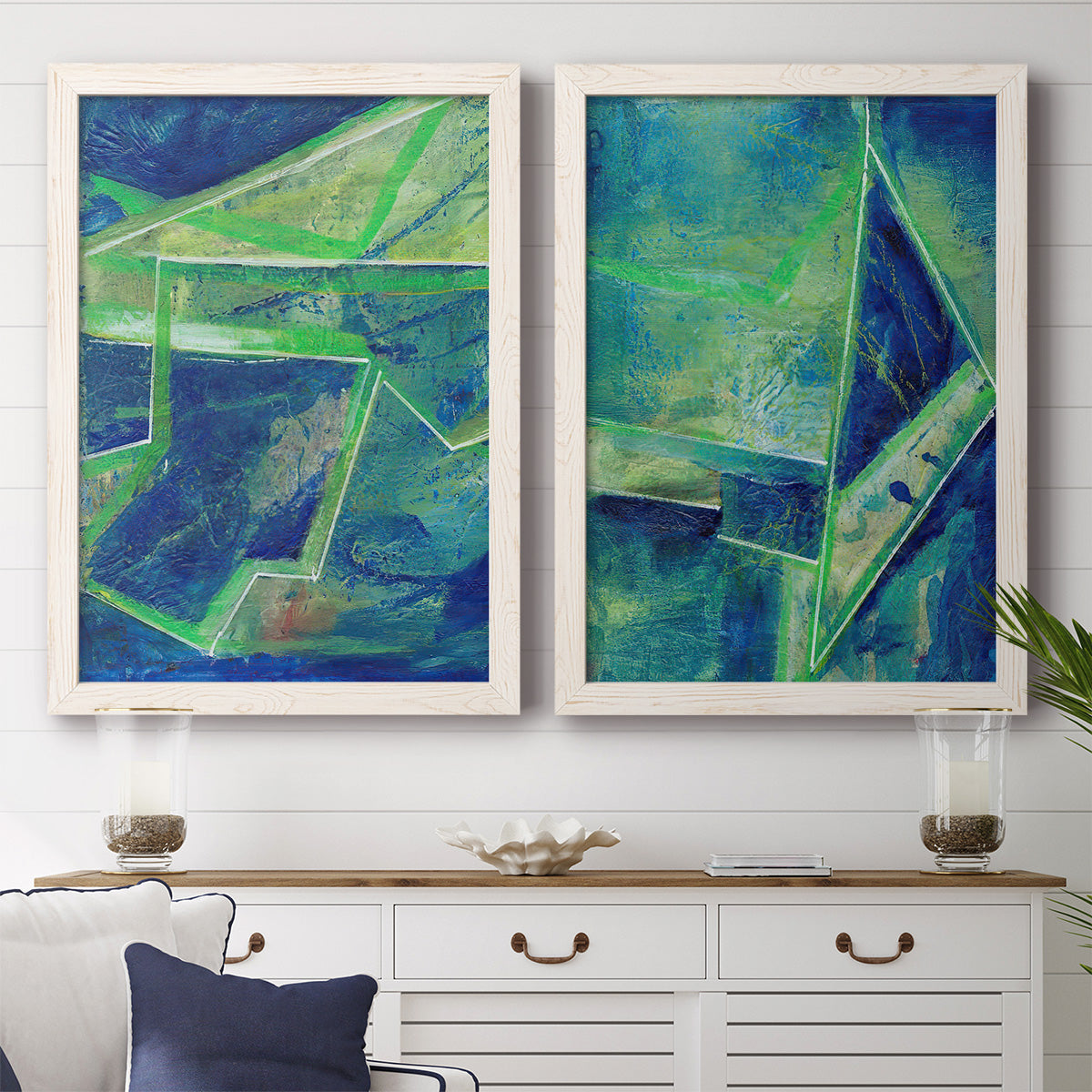 Set of two white barnwood framed canvas prints depicting a coordinated art pair of interlocking blue and green angular forms rendered as textured geometric abstracts above a dining room sideboard.