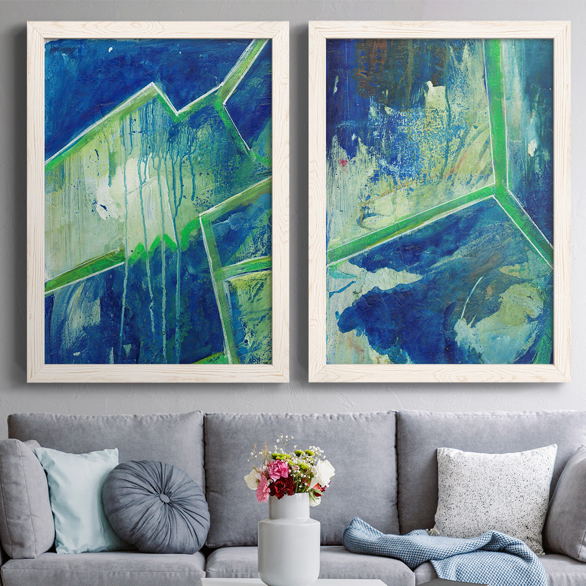 Set of two white barnwood framed canvas prints depicting paired textured geometric abstracts with deep cobalt fields, bright green edges, and layered linear facets above a sofa in a contemporary living room.