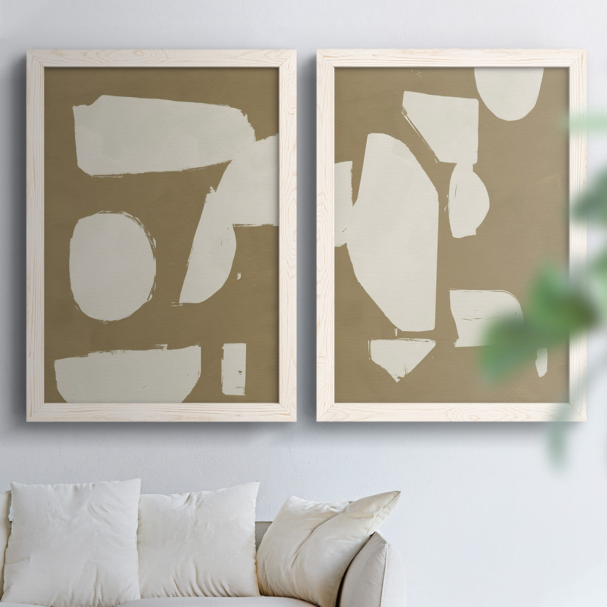 Set of two white barnwood framed canvas prints depicting flat blocky forms, rough painted edges, and strong negative space arranged across two complementary compositions above a sofa in a bright living space.