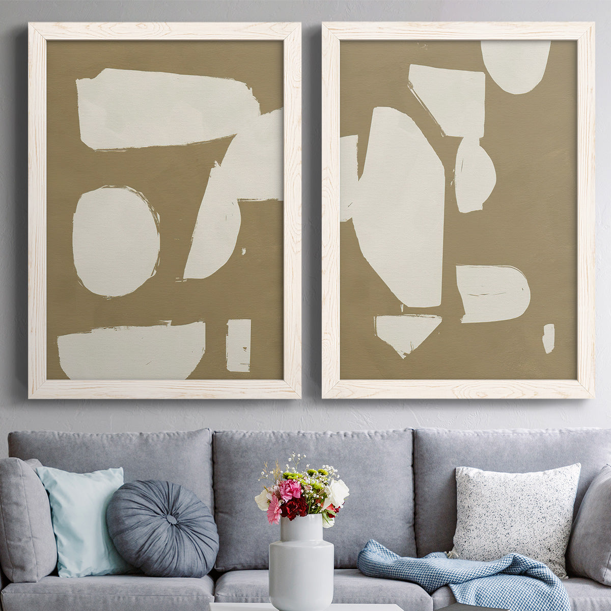 Set of two white barnwood framed canvas prints depicting paired bold minimalist shape abstracts with flat blocky forms, rough painted edges, and strong negative space above a sofa in a contemporary living room.