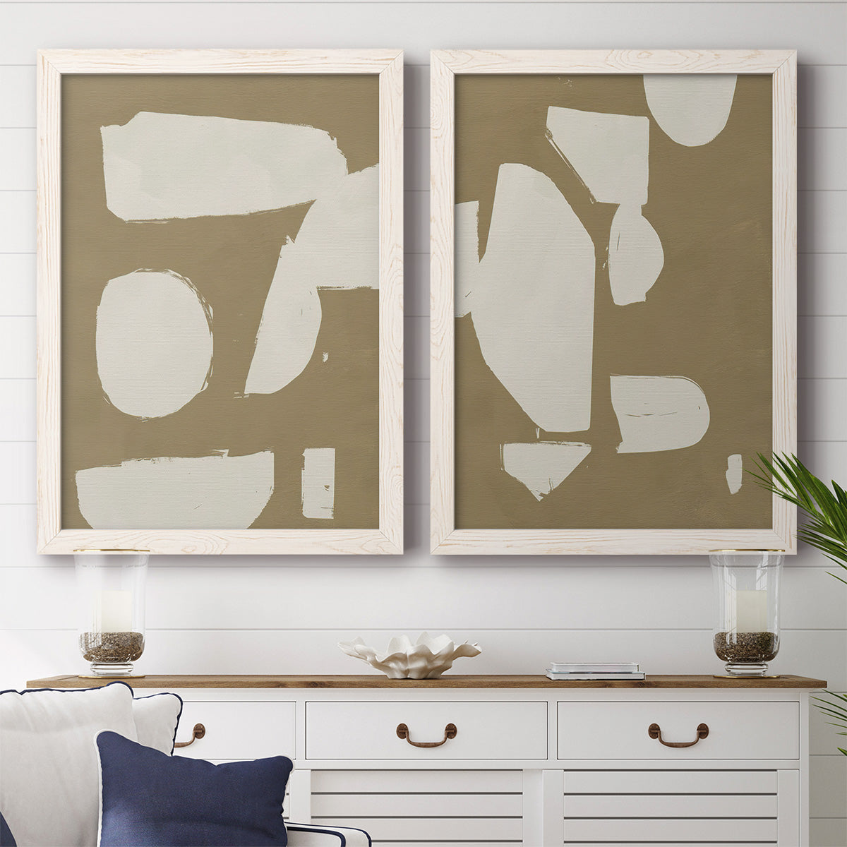 Set of two white barnwood framed canvas prints depicting a coordinated art pair of irregular white cutout-like shapes on taupe grounds rendered as bold minimalist shape abstracts above a dining room sideboard.