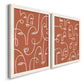 Angled view of a set of two white barnwood framed canvas prints featuring two graphic portrait patterns featuring many continuous-line faces across terracotta grounds.
