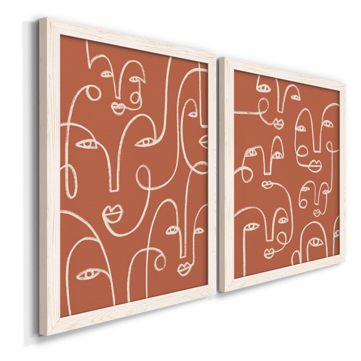 Angled view of a set of two white barnwood framed canvas prints featuring two graphic portrait patterns featuring many continuous-line faces across terracotta grounds.