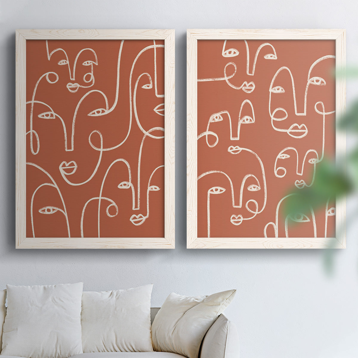 Set of two white barnwood framed canvas prints depicting white outlined features, repeated profiles, and playful clustered expressions arranged across two complementary compositions above a sofa in a bright living space.