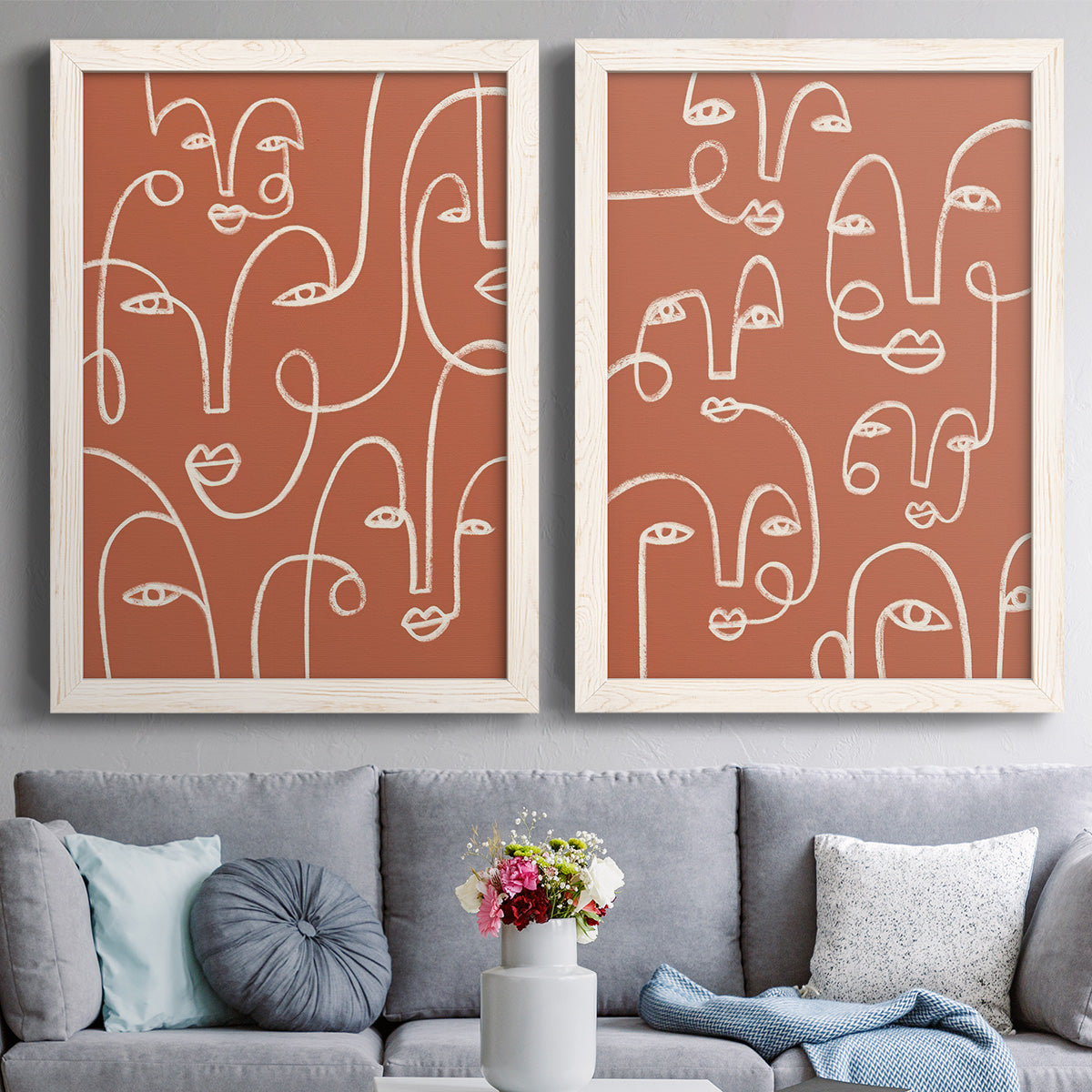 Set of two white barnwood framed canvas prints depicting paired graphic portrait patterns with white outlined features, repeated profiles, and playful clustered expressions above a sofa in a contemporary living room.
