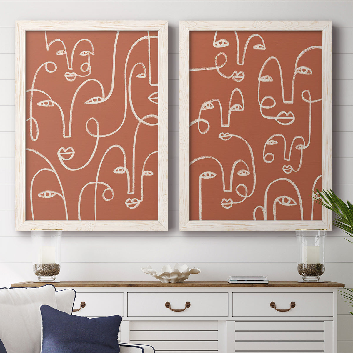 Set of two white barnwood framed canvas prints depicting a coordinated art pair of many continuous-line faces across terracotta grounds rendered as graphic portrait patterns above a dining room sideboard.