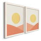 Angled view of a set of two white barnwood framed canvas prints featuring two minimalist boho landscapes featuring yellow suns rising over terracotta geometric hills.