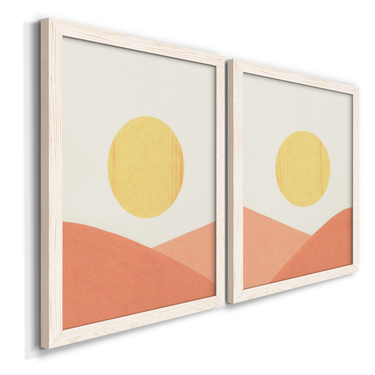 Angled view of a set of two white barnwood framed canvas prints featuring two minimalist boho landscapes featuring yellow suns rising over terracotta geometric hills.