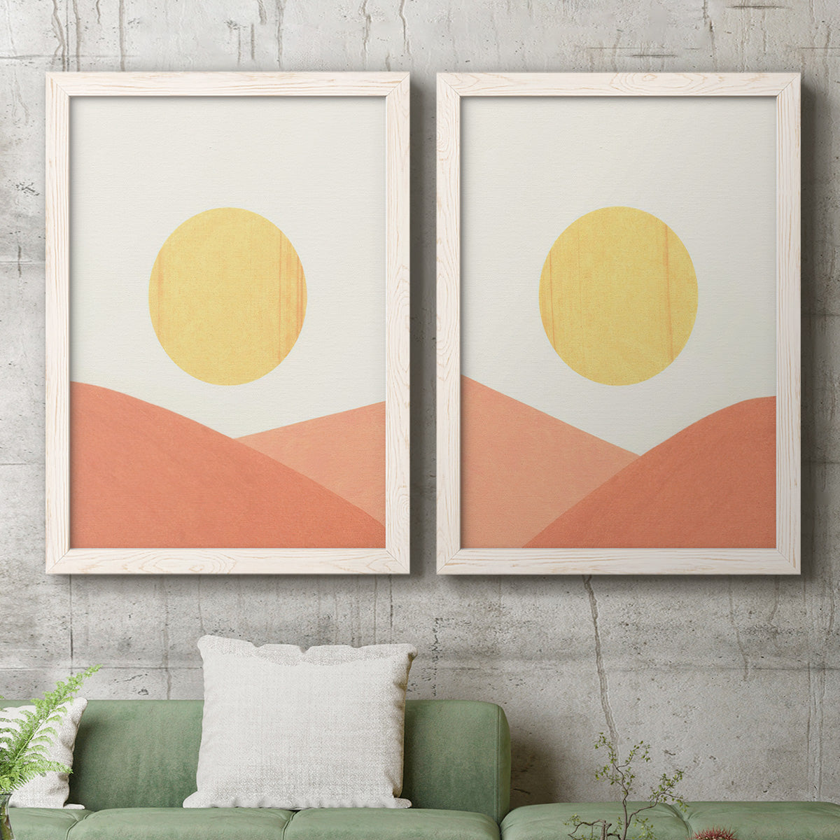 Set of two white barnwood framed canvas prints depicting a coordinated art pair of yellow suns rising over terracotta geometric hills rendered as minimalist boho landscapes above a sofa in a modern living room.