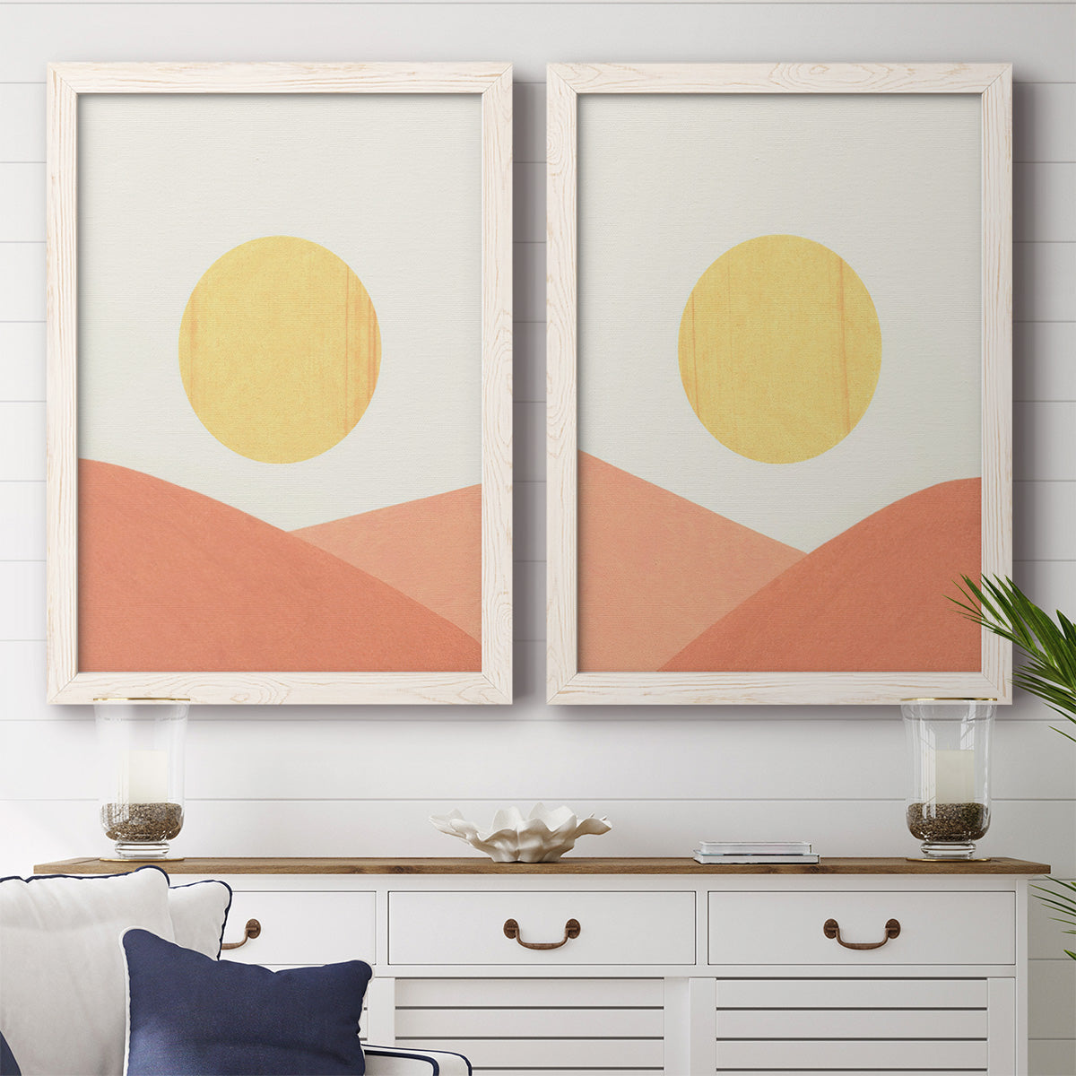 Set of two white barnwood framed canvas prints depicting a coordinated art pair of yellow suns rising over terracotta geometric hills rendered as minimalist boho landscapes above a dining room sideboard.