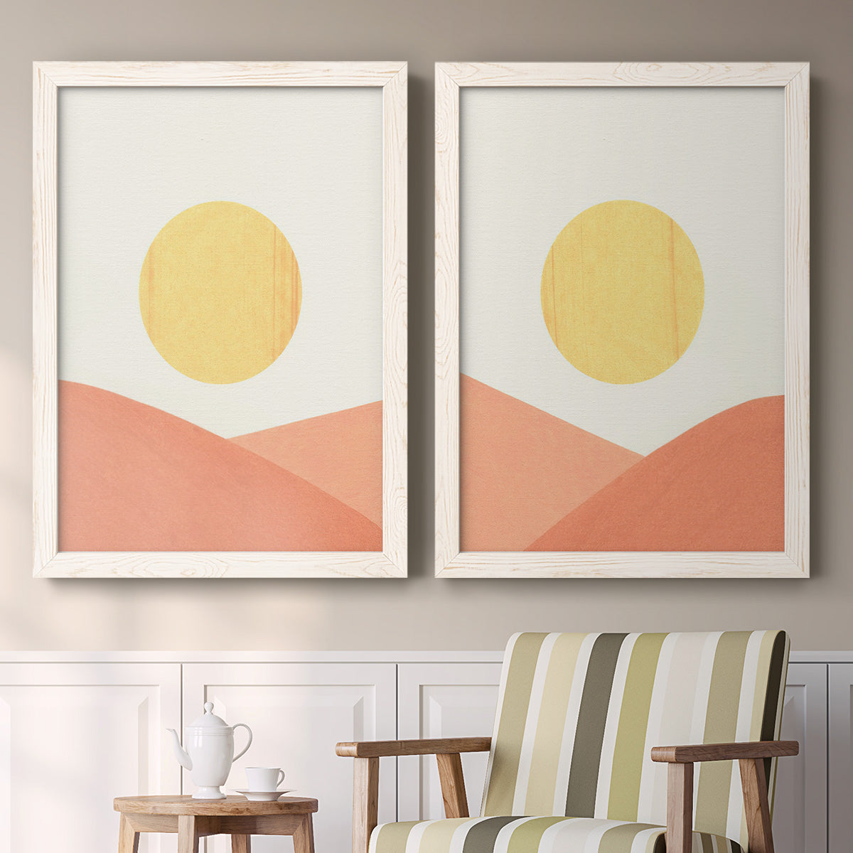 Set of two white barnwood framed canvas prints depicting two minimalist boho landscapes featuring yellow suns rising over terracotta geometric hills above a sideboard in a cozy sitting room.