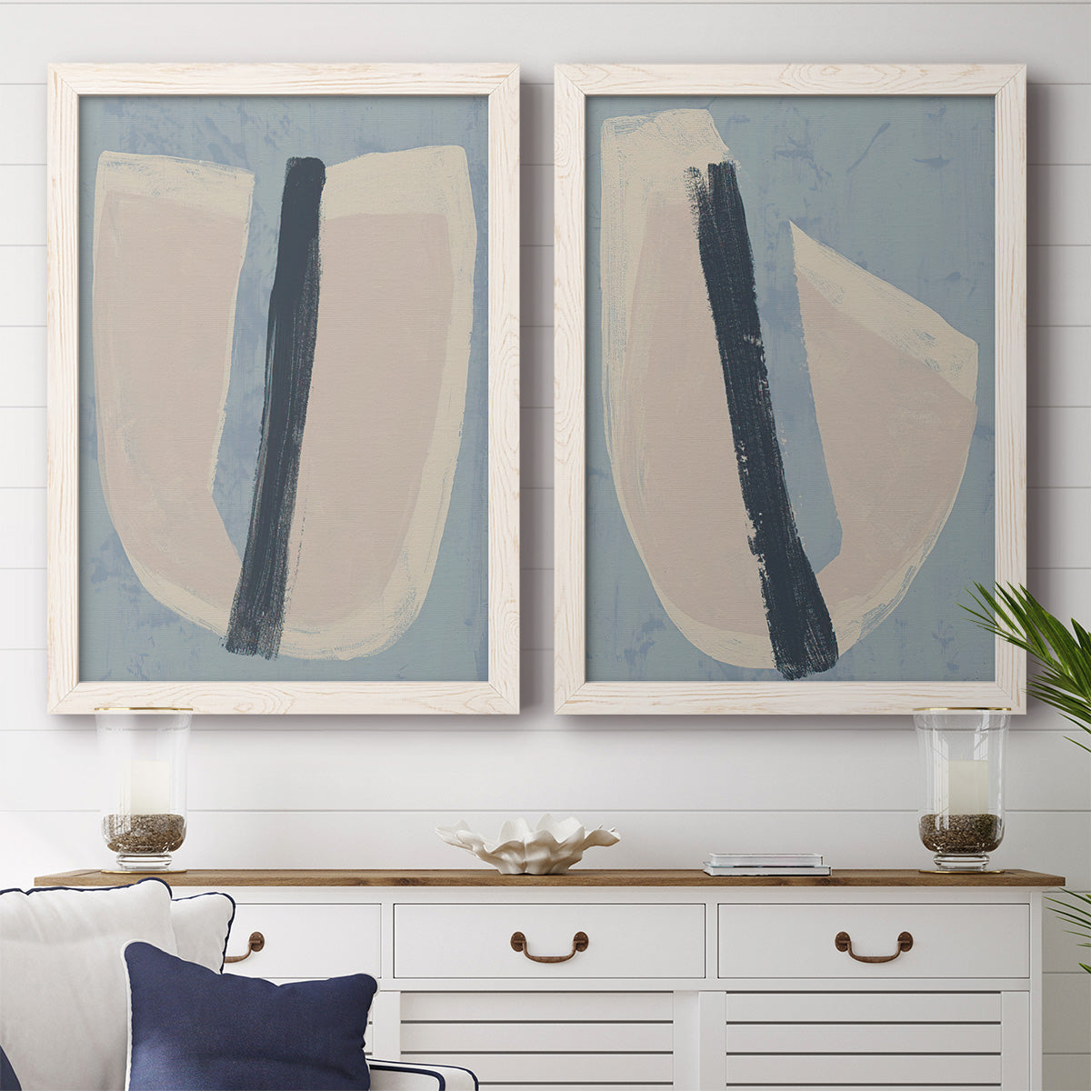 Set of two white barnwood framed canvas prints depicting a coordinated art pair of single navy brush slashes across layered paper-like shapes rendered as minimalist collage-style abstracts above a dining room sideboard.