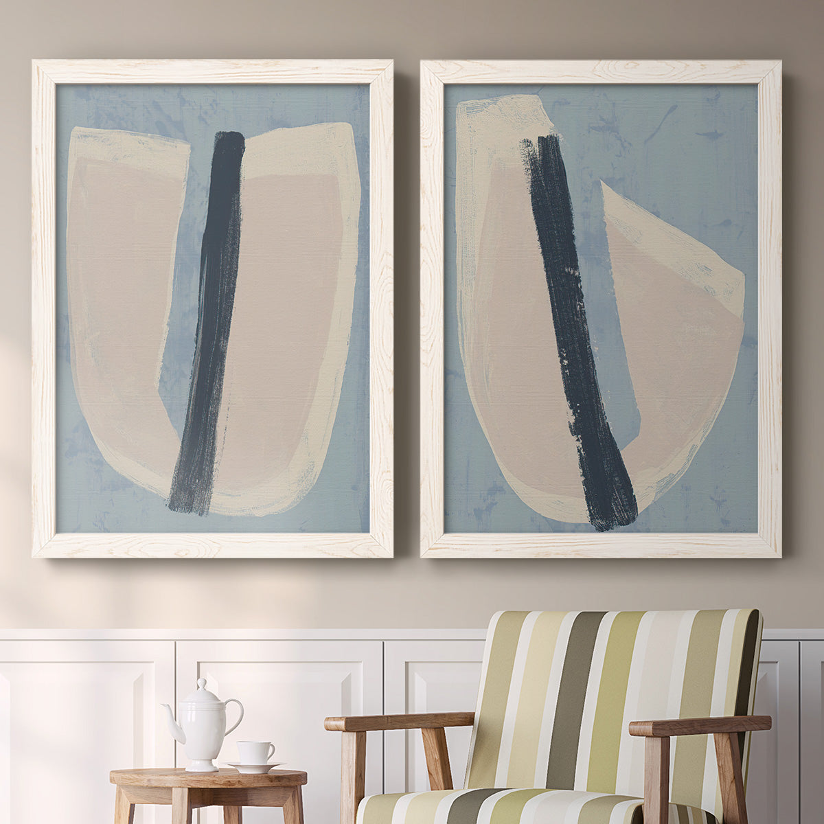 Set of two white barnwood framed canvas prints depicting two minimalist collage-style abstracts featuring single navy brush slashes across layered paper-like shapes above a sideboard in a cozy sitting room.