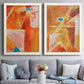 Set of two white barnwood framed canvas prints depicting paired warm geometric abstracts with white dividing lines, small turquoise accents, and layered painted texture above a sofa in a contemporary living room.