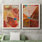 Set of two white barnwood framed canvas prints depicting a coordinated art pair of faceted rust orange and coral geometric fields rendered as warm geometric abstracts above a sofa in a modern living room.