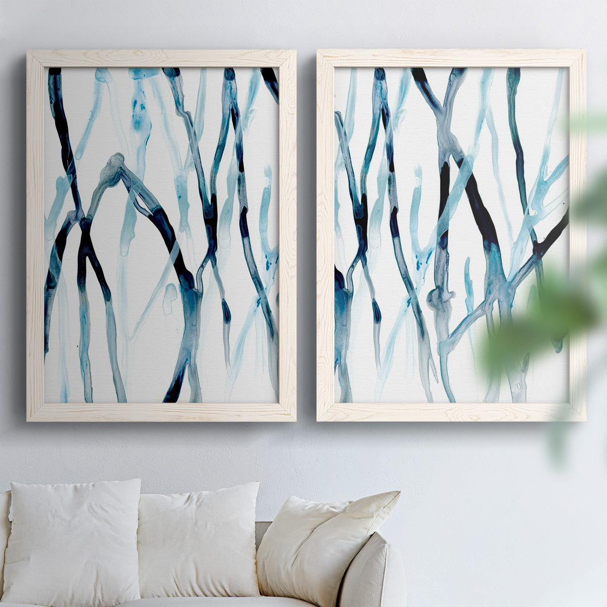 Set of two white barnwood framed canvas prints depicting slender vein-like strokes, transparent overlaps, and open negative space arranged across two complementary compositions above a sofa in a bright living space.
