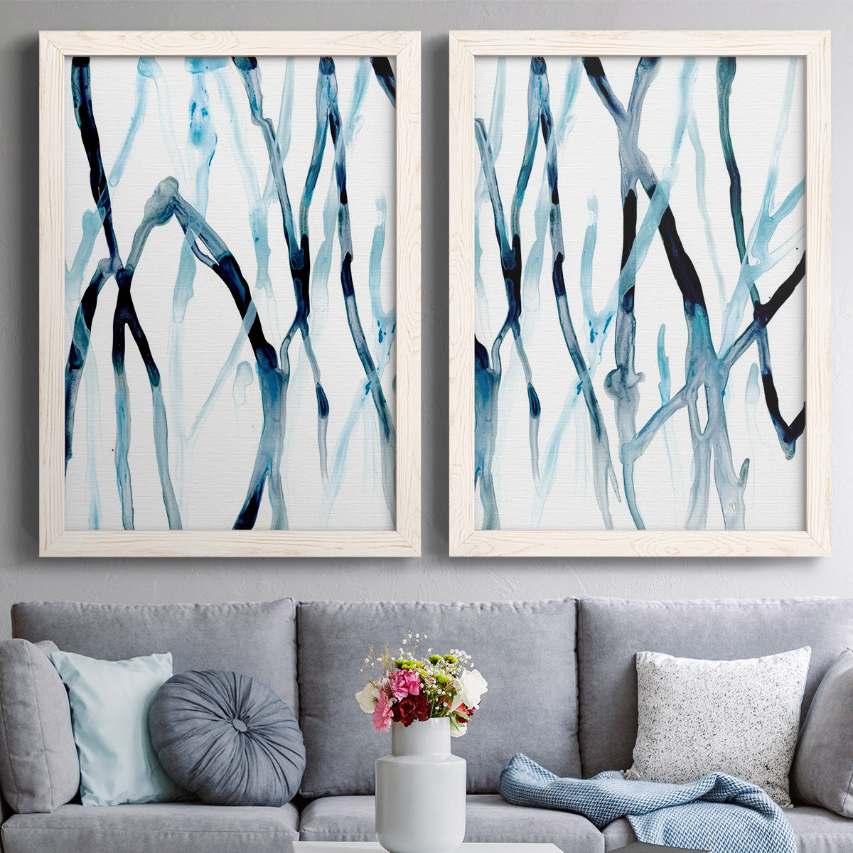 Set of two white barnwood framed canvas prints depicting paired fluid organic abstracts with slender vein-like strokes, transparent overlaps, and open negative space above a sofa in a contemporary living room.