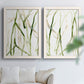 Set of two white barnwood framed canvas prints depicting slender vein-like strokes, transparent overlaps, and open negative space arranged across two complementary compositions above a sofa in a bright living space.