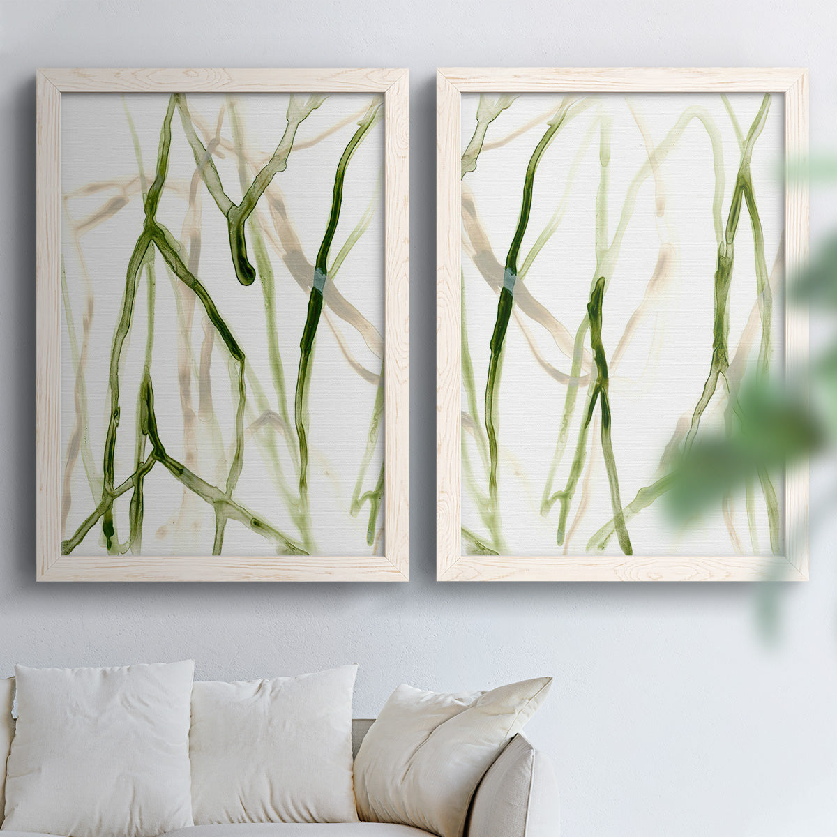 Set of two white barnwood framed canvas prints depicting slender vein-like strokes, transparent overlaps, and open negative space arranged across two complementary compositions above a sofa in a bright living space.