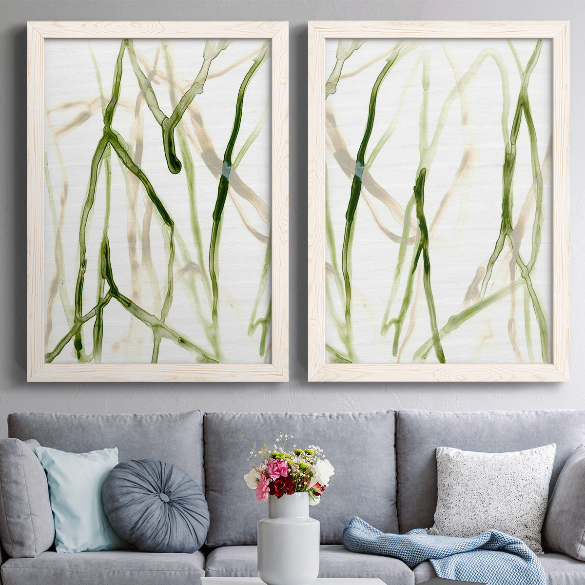 Set of two white barnwood framed canvas prints depicting paired fluid organic abstracts with slender vein-like strokes, transparent overlaps, and open negative space above a sofa in a contemporary living room.