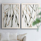 Set of two white barnwood framed canvas prints depicting slender vein-like strokes, transparent overlaps, and open negative space arranged across two complementary compositions above a sofa in a bright living space.